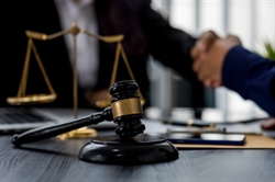 [ai] A wooden gavel on a table with a blurred background showing people shaking hands and legal scales, symbolizing a legal agreement or negotiation.